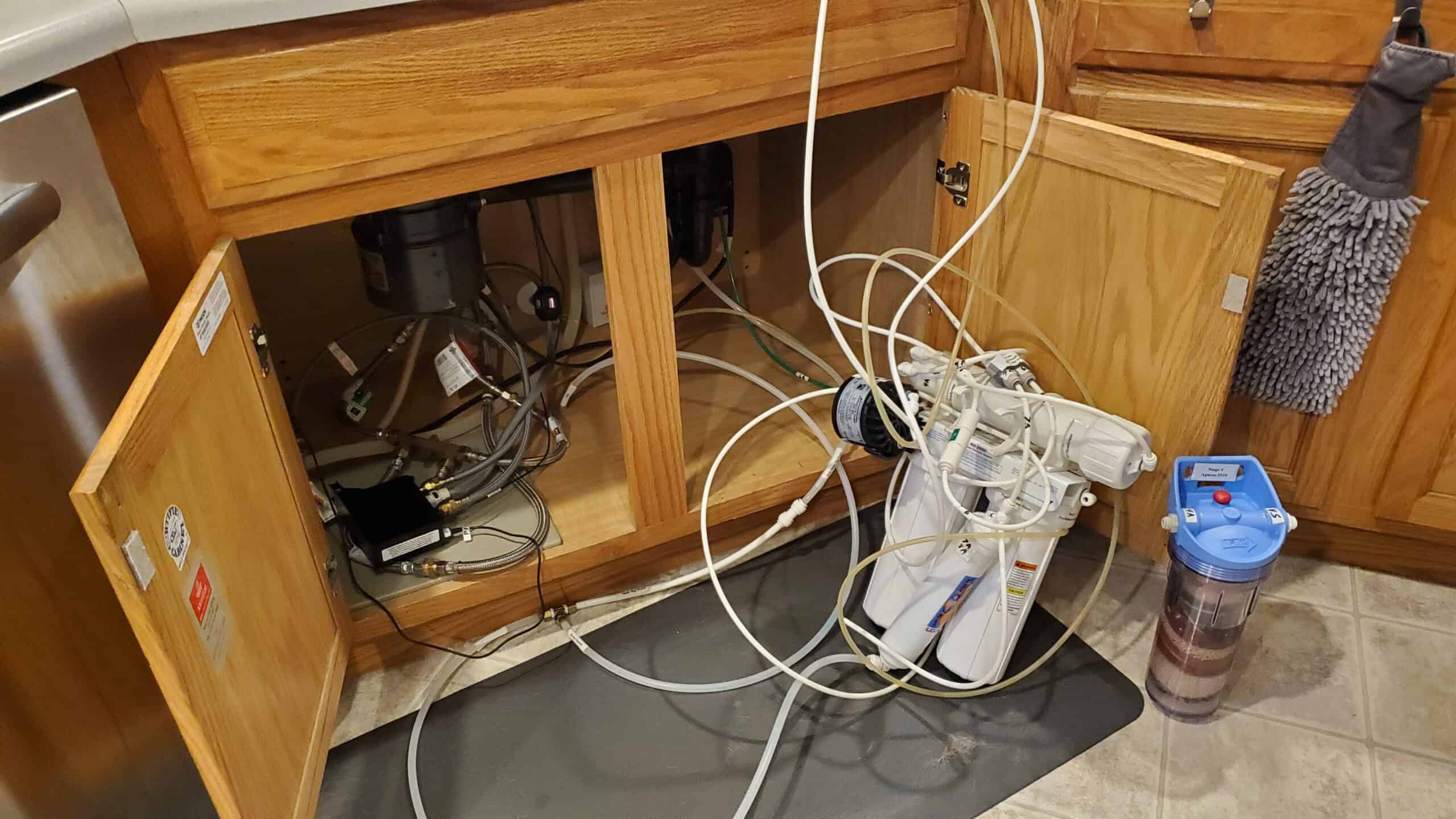 Alternate water filter setup with exposed pipes and wires under kitchen sink.