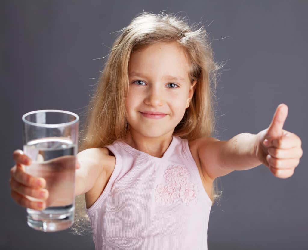 Young girl holding a glass of water and giving a thumbs up to represent confidence in clean, safe drinking water.
