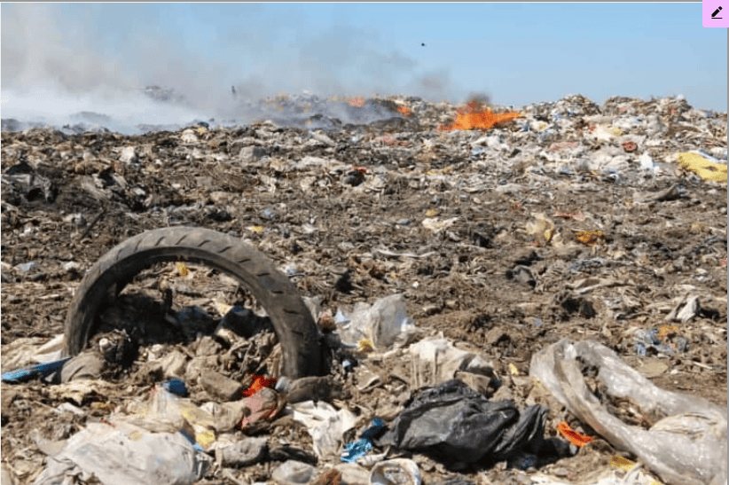Image of trash and debris pollution in a landfill with burning waste in the background, highlighting water pollution issues.