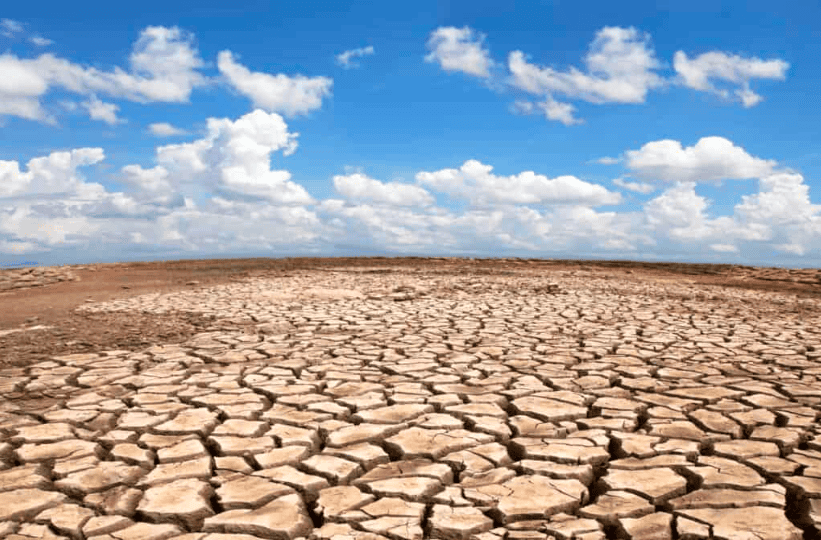 Dry cracked earth under blue sky with clouds.