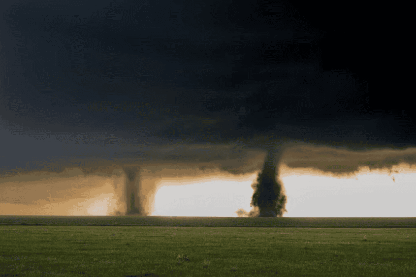 Tornado storm forming on flat grassland under dark ominous sky.