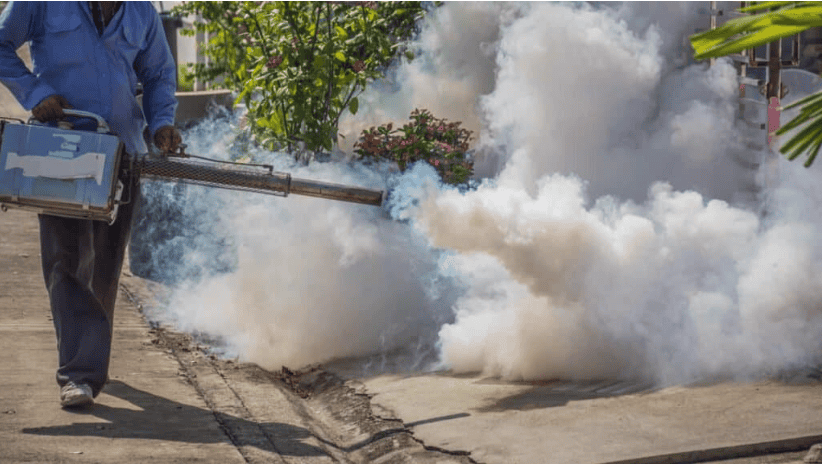 A person uses a water misting device for pest control outdoors.